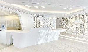 Vestíbulo de oficina moderno con mostrador de recepción curvilíneo blanco hecho de superficie sólida y paredes divisorias perforadas.