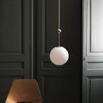 Un solo sistema eléctrico de colgante con una pantalla redonda blanca colgante frente a puertas paneladas oscuras, al lado de una silla marrón minimalista