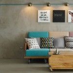 Una sala de estar moderna con una pared de concreto con un sofá colorido adornado con varios cojines estampados, una mesa auxiliar de madera y una decoración montada en la pared que incluye una obra de arte del alfabeto y un retrato de un animal después de cambiar la instalación.