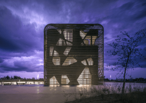 Edificio moderno con una intrincada fachada de celosía iluminada desde dentro contra un espectacular cielo nocturno, seleccionado como finalista del Premio de Arquitectura AZ.