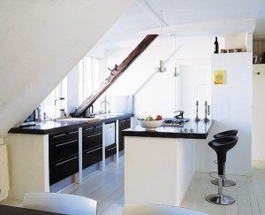 Una cocina abierta y moderna con paredes blancas, mobiliario negro en dos frentes y electrodomésticos de acero inoxidable, que cuenta con una barra.