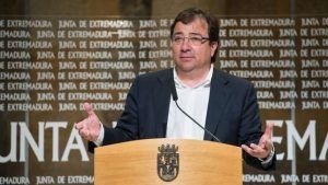 Un hombre con gafas y traje oscuro se encuentra en un podio con el emblema de la Junta de Extremadura, dirigiéndose a un público sobre el "Plan de Rehabilitación y Vivienda