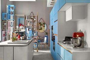 Una cocina moderna con gabinetes azules y blancos, electrodomésticos de acero inoxidable y detalles decorativos en rojo exhibidos en Casa Decor 2016.