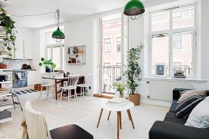 Sala de estar moderna y luminosa con área de comedor, grandes ventanales y paredes blancas, acentuadas con lámparas colgantes verdes y plantas de interior, que exudan "mucha vida" en cada rincón de este acogedor