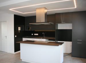 Una cocina moderna con gabinetes negros, iluminación integrada y una isla central, sometida a una reforma integral.