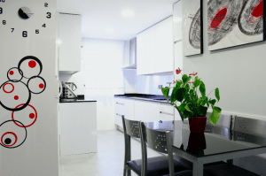 Una reforma integral de la cocina con gabinetes blancos, una encimera oscura y un pequeño espacio de comedor con una mesa gris y sillas, acentuado.