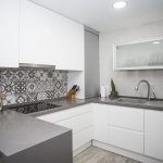 Una reforma de cocina moderna con gabinetes blancos, encimeras grises y un protector contra salpicaduras de azulejos decorativos.
