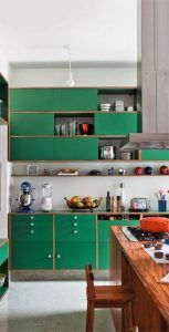 Una cocina compacta en Madrid, con armarios verdes, electrodomésticos de acero inoxidable y una variedad de utensilios de cocina ordenadamente dispuestos en estantes.