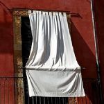 Soluciones ecoeficientes: Cortinas blancas, diseñadas para brindar frescura, ondean desde una ventana abierta en un edificio con paredes rojas.