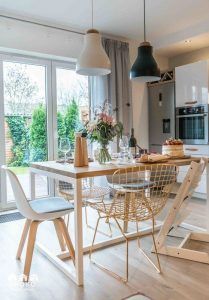 Un comedor moderno con una mesa de madera preparada para comer, que presenta una combinación de estilos de sillas, luces colgantes y vista al jardín. Este espacio ha sido recientemente reformado integralmente.