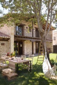 Una tranquila ambientación exterior que presenta una casa de piedra de dos pisos con un balcón de madera, destinada a la renovación de casas, un comedor metálico.