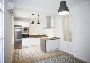 Un interior de cocina moderno con electrodomésticos de acero inoxidable, gabinetes blancos, una cocina cerrada con fregadero y luces colgantes.