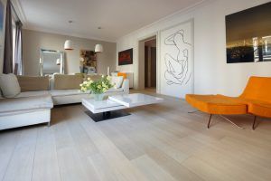Moderna sala de estar con paredes neutras, un sofá blanco, una silla vibrante naranja, una mesa de café blanca, arte contemporáneo y decoración del