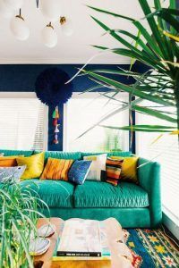Una sala de estar de colores brillantes que sigue las tendencias para con un sofá verde adornado con almohadas multicolores, una alfombra estampada y una planta de otoño en maceta en primer plano.