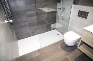 Cuarto de baño moderno con azulejos grises, destacando una ducha a ras de suelo, un inodoro montado en la pared y un tocador de