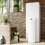 Un enfriador de agua de suelo colocado en una habitación bien iluminada con una pared decorativa de piedra, junto a muebles de mimbre y plantas de interior, integra la climatización del futuro.