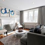 Un salón contemporáneo con tonos neutros, que cuenta con un sofá gris, sillones de acento, una mesa de café circular y elementos decorativos complementados por una