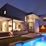 Descripción modernizada: Reformas energéticas en una casa de dos pisos iluminada al anochecer con una piscina en primer plano diseñado para ahorrar energía.