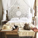 Una habitación matrimonial bien adornada que cuenta con una gran cama con dosel blanco, cabecero blanco ornamentado y accesorios decorativos, incluidos un sombrero de