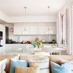 Una cocina abierta, moderna con gabinetes blancos y electrodomésticos de acero inoxidable, acentuada con iluminación colgante y con una is