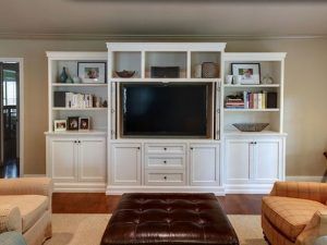 Una sala de estar con un gran mueble de televisión blanco incorporado que alberga un televisor de pantalla plana negro, flanqueado por estantes y gabinetes,