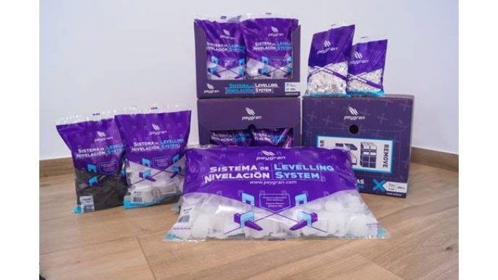 Productos del sistema nivelador de baldosas expuestos sobre suelo de madera, compuestos por varios paquetes y cajas de Peygran.
