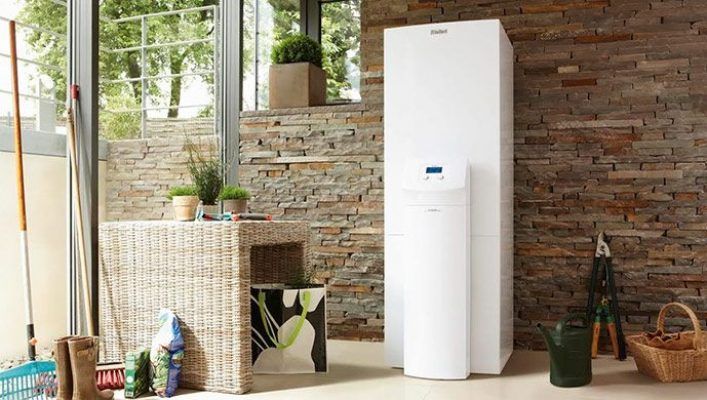Un enfriador de agua de suelo colocado en una habitación bien iluminada con una pared decorativa de piedra, junto a muebles de mimbre y plantas de interior, integra la climatización del futuro.