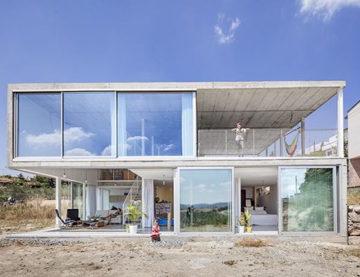 Casa moderna de dos plantas con grandes ventanales de cristal y un balcón individual en la parte superior, construida por menos de 900 euros el m2.