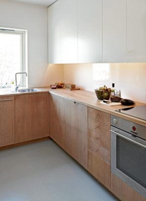 Una cocina moderna con gabinetes de madera clara, encimeras blancas, electrodomésticos integrados y una iluminación sutil en el salpicadero, perfecta