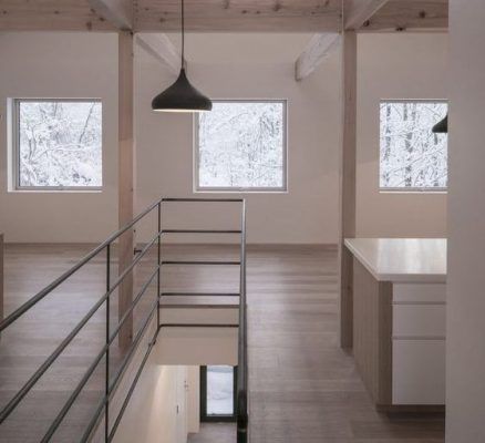 Interior de un piso de segunda mano minimalista con suelos y paredes de madera, una escalera a la izquierda, un mostrador de cocina a la derecha y nie