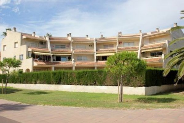 Descripción: Una fila de casas adosadas con balcones en Cambrils, dispuestas frente a un cielo despejado, delimitadas por un seto bien cuid