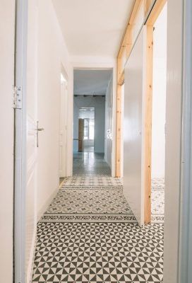 Un pasillo estrecho en una casa con suelo de baldosas con motivos geométricos, paredes blancas y marcos de puertas de madera preparados para decorar.