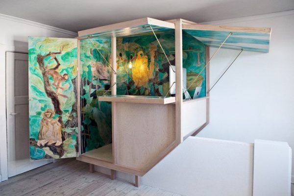 Un cubículo ingeniosamente pintado con murales de temática forestal que representan varios animales, instalado en una habitación con piso de madera clara, ejemplifica los espacios transformables.