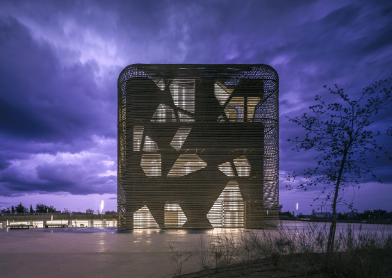 Edificio moderno con una intrincada fachada de celosía iluminada desde dentro contra un espectacular cielo nocturno, seleccionado como finalista del Premio de Arquitectura AZ.