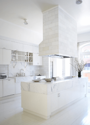 Una brillante y moderna cocina en la casa de Nueva York, con gabinetes blancos, encimeras de mármol y una gran isla central bajo una campana.