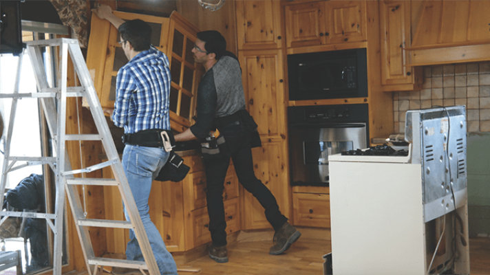 Dos gemelos, Drew y Jonathan Scott, con cinturones de herramientas están trabajando en el interior de la cocina de madera de la casa de mis sueños, con uno subiendo una escalera.