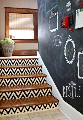 Una escalera con barrotes decorativos, adyacente a una pared de pizarrón con marcos decorativos y una planta, dentro de una casa.