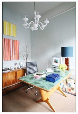 Una oficina moderna en casa con un escritorio de estilo mediados de siglo, una silla elegante, una lámpara de araña arriba y acentos de decoración.