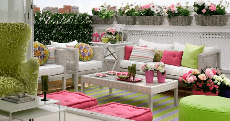 Una terraza al aire libre, siguiendo las nuevas tendencias para mobiliario exterior, está adornada con muebles de colores vivos en blanco y rosa, cojines a