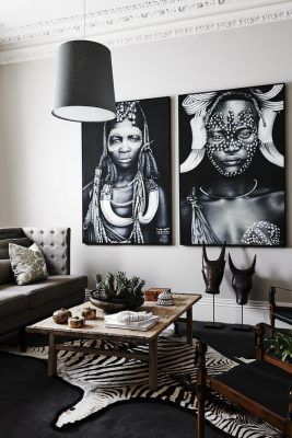 Una sala de estar con estilo que presenta una decoración africana mediante un esquema de colores monocromático, con dos grandes retratos en blanco y negro en la pared, un alf.