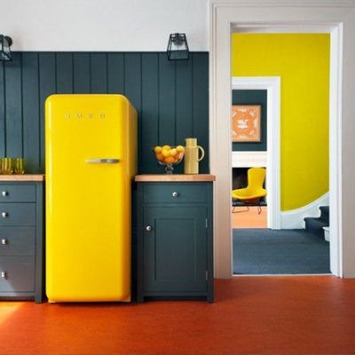 Un refrigerador amarillo de estilo retro se encuentra en una cocina con gabinetes de color gris oscuro, complementado con vibrantes detalles en amarillo y naranja en las habitaciones contiguas, ideal para quienes buscan reformar el piso.