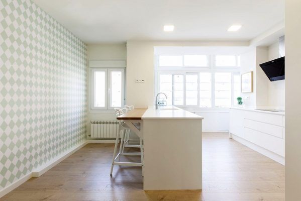 Un espacio moderno que incluye una cocina brillante con gabinetes blancos, una isla con taburetes de bar y un tapiz de papel de patrón geométrico.