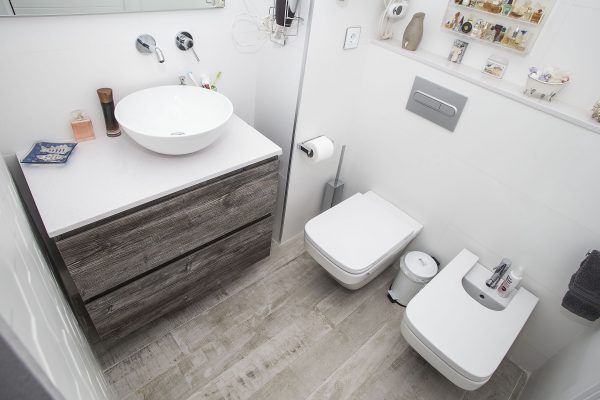 Una moderna decoración de baños interior con un lavabo montado en la pared junto a un tocador, un inodoro y bidé, con suelo de baldosas y pared.