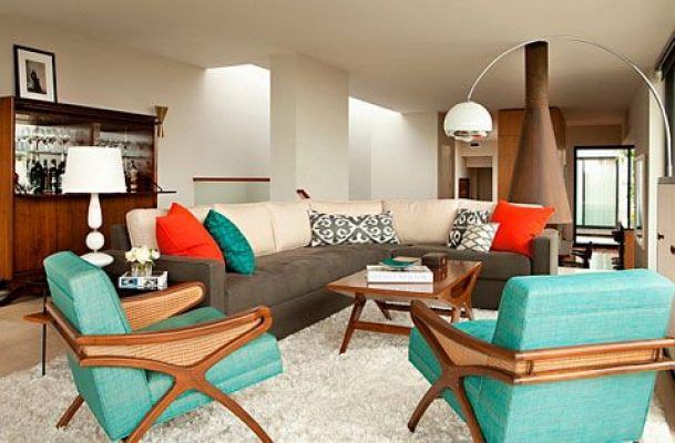 Un salón moderno con colores vivos, destacando un sofá gris acentuado con cojines rojos, dos sillones color turquesa, una alfombra