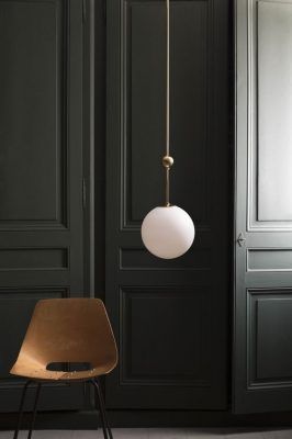 Un solo sistema eléctrico de colgante con una pantalla redonda blanca colgante frente a puertas paneladas oscuras, al lado de una silla marrón minimalista