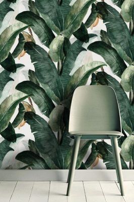 Una silla moderna frente a un papel tapiz con estampado de hojas tropicales agrega un toque fresco a las tendencias de decoración primaveral.