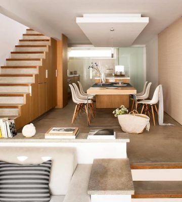 Una cocina moderna con elementos de madera y un comedor, diseñada por Cotacero Taller de Arquitectura, cuenta con una escalera flotante a la izquierda y un acogedor rincón para sentarse en el