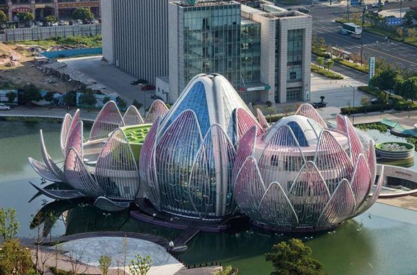 Un edificio de arquitectura moderna que se asemeja a una flor de loto situada al lado de un cuerpo de agua con un paisaje urbano circundante.