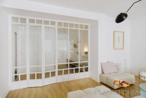 Una decoración brillante y minimalista en el salón con paredes blancas, destacando un sofá rosa claro, redondos otomanos beige, una mesa de centro redonda.