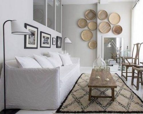 Un salón moderno diseñado para la optimización del espacio, caracterizado por un sofá blanco con numerosos cojines, una mesa de café de madera y una alfombra.